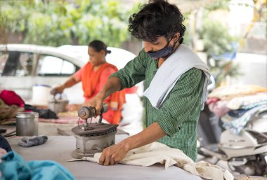 A LABOURER IRONING CLOTHES WEARING FACE MASK clipart