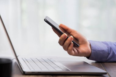 İnsan eli telefonun önünde dizüstü bilgisayarla çalışıyor..