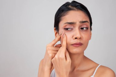 A young woman popping a pimple on her face. clipart