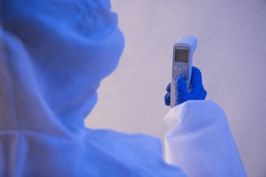 A health worker in PPE kit holding a temperature checking gun. clipart