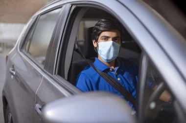 Arabasında maskesiyle oturan genç bir adam..