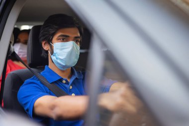 Arabasını kullanan yüz maskeli genç bir adam..