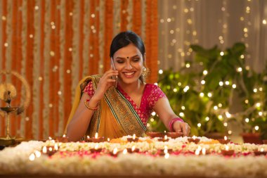 Genç bir kız telefonda konuşurken diwali diyas yerleştiriyor.
