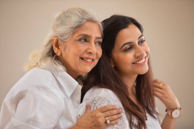 A SENIOR MOTHER AND ADULT DAUGHTER LOOKING AWAY AND POSING TOGETHER clipart