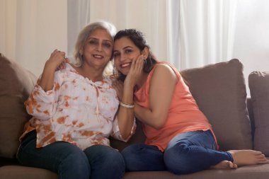 SOFA 'nın üzerinde oturan ve CAMERA' ya gülümseyen bir anne ve kız.