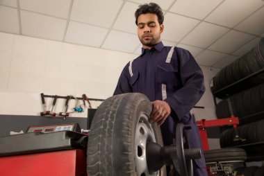 Technician doing wheel balancing of a tyre at a tyre shop clipart