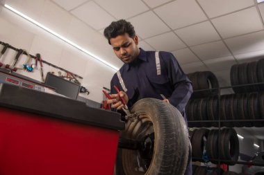 Technician doing wheel balancing of a tyre at a tyre shop clipart