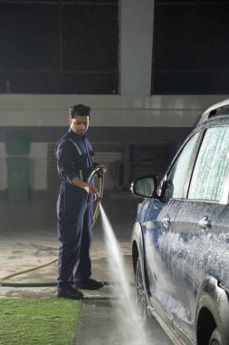 Teknisyen araba yıkamada yüksek basınçlı çamaşır makinesiyle arabayı temizliyor.