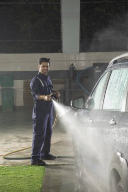 Teknisyen araba yıkamada yüksek basınçlı çamaşır makinesiyle arabayı temizliyor.