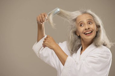 Saçını fırçayla tarayan mutlu yaşlı bir kadın..