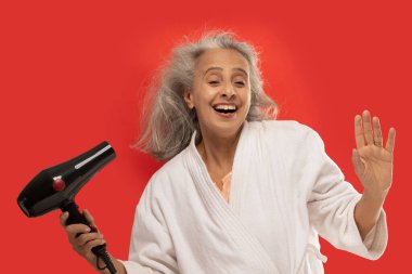 Saçını kurutma makinesiyle kurutan mutlu yaşlı bir kadın..