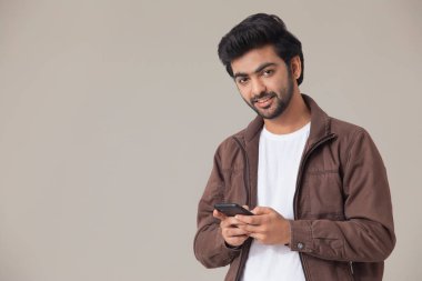 CAMERA 'ya bakan ve mobil telefon kullanırken gülümseyen genç bir adam.