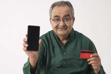 AN OLD MAN HOLDING MOBILE PHONE AND DEBIT CARD IN FRONT OF CAMERA clipart