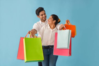 Modellik yapan bir çift, alışveriş çantalarını taşırken birbirlerine sevgiyle bakıyor.