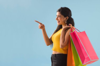 A young woman standing with Carrybags pointng elsewhere. clipart