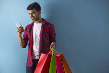 Cep telefonuna bakarken yanında çantalarla duran genç bir adam.