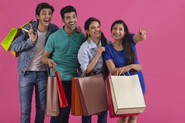 A girl pointing elsewhere amidst  group of youngsters standing happily holding their carrybags. clipart