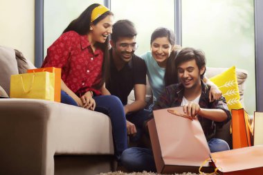 Oturma odasında arkadaşlarına alışverişini gösteren genç bir adam..