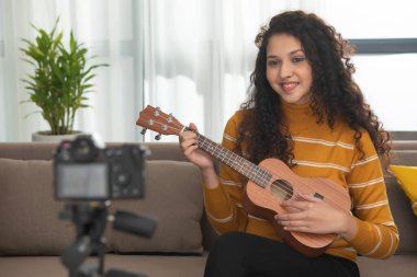 A HAPPY TEENAGE GIRL PLAYING UKELELE IN FRONT OF CAMERA AND RECORDING IT clipart