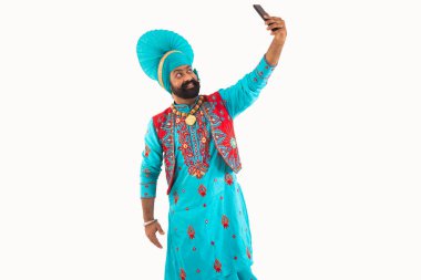 A man in Bhangra Costume taking a selfie in his phone. clipart