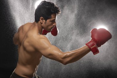 Karanlık bir arka planın önünde boks eldiveni giymiş bir adam havaya yumruk atıyor.,