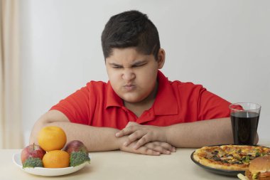 Genç çocuk öfkeyle meyve ve sebzelere bakıyor (Obezite)