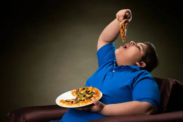 Kanepede oturup pizza yiyen genç bir çocuk.)