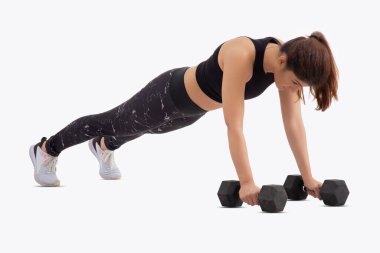 Beyaz arka planda dambıllarla şınav çeken bir kadın..