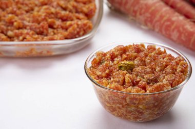 Gajar ka halwa in a glass bowl kept in front of carrots and a serving bowl. clipart