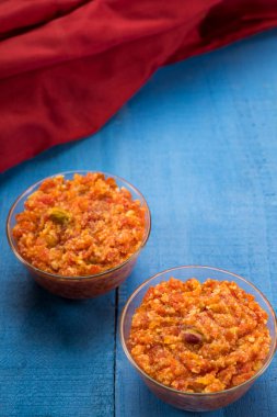 Gajar ka halwa in two glass bowls kept next to a red cloth. clipart