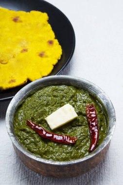 Delicious bowl of sarso ka saag with makki ki roti kept on a table. clipart