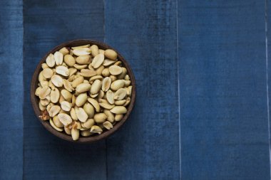 Mavi ahşap bir masada, ahşap bir kasede saklanmış sade fıstıklar..