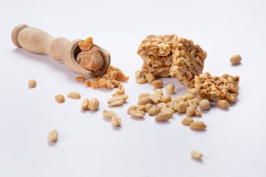 Tahta kaşıkta jaggery Mungfali chikki ve beyaz arka planda sade fıstıkla saklanır..