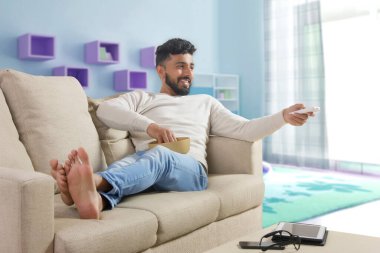 Genç adam kanepede dinleniyor ve televizyon izliyor..