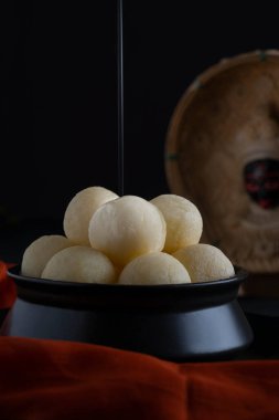 Close up of mouth watering white rasgullas kept in a black bowl with sugar syrup dripping on top. clipart