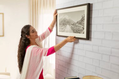 Portrait of a single woman fixing a photo frame at her home. clipart