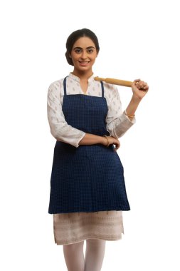 Portrait of a single woman wearing an apron holding a rolling pin in hand. clipart