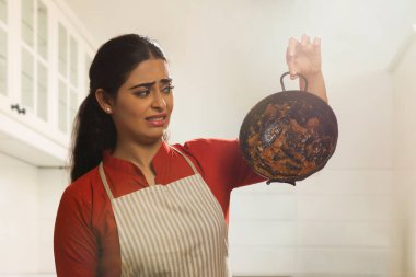 Portrait of a single woman wearing an apron and holding dirty utensil in hand. clipart