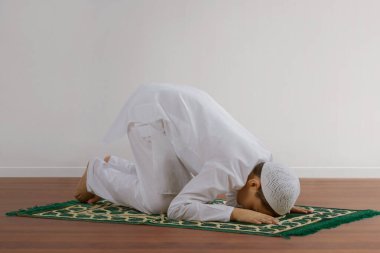 Müslüman çocuk yerde oturmuş dua ediyor.