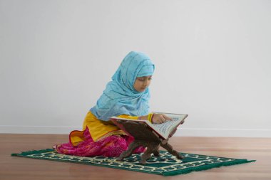 Young Muslim girl wearing hijab reciting namaz from quran on the occasion of eid clipart