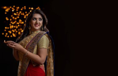 Sari giymiş bir kadın para tutuyor ve gülümsüyor.