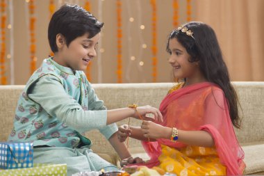 Little girl tying Rakhi to her brother on Rakshabandhan clipart