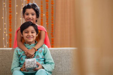 Erkek ve kız kardeş ellerinde hediye kutusuyla gülümsüyor.