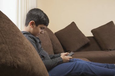 Çocuk kanepede oturuyor ve oturma odasında akıllı telefon kullanıyor.