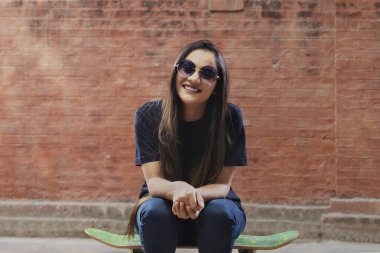 Sokağın kaykayında oturan genç ve güzel bir kadın. Güneş gözlüğü takıyor.