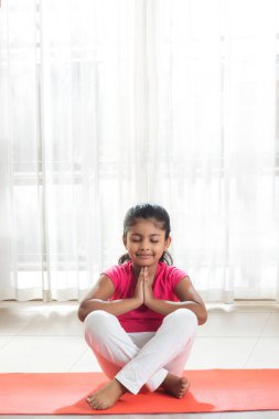 Evde yoga minderinde dua eden küçük bir kız.