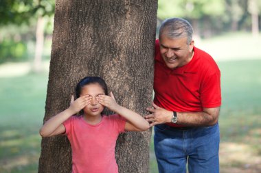 Büyükbaba ve torun parkta saklambaç oynuyorlar.