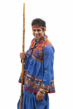 Portrait of happy young man in traditional wear holding stick against white background clipart