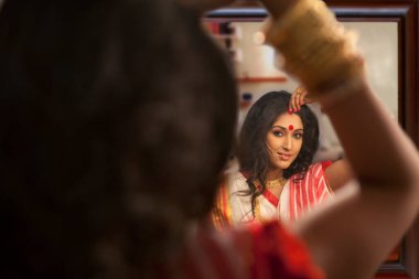 Bengali woman putting sindoor on her forehead clipart