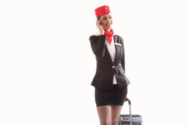 Beyaz arka planda izole edilmiş bagaj çantasını çekerken cep telefonu kullanan bir hostes.